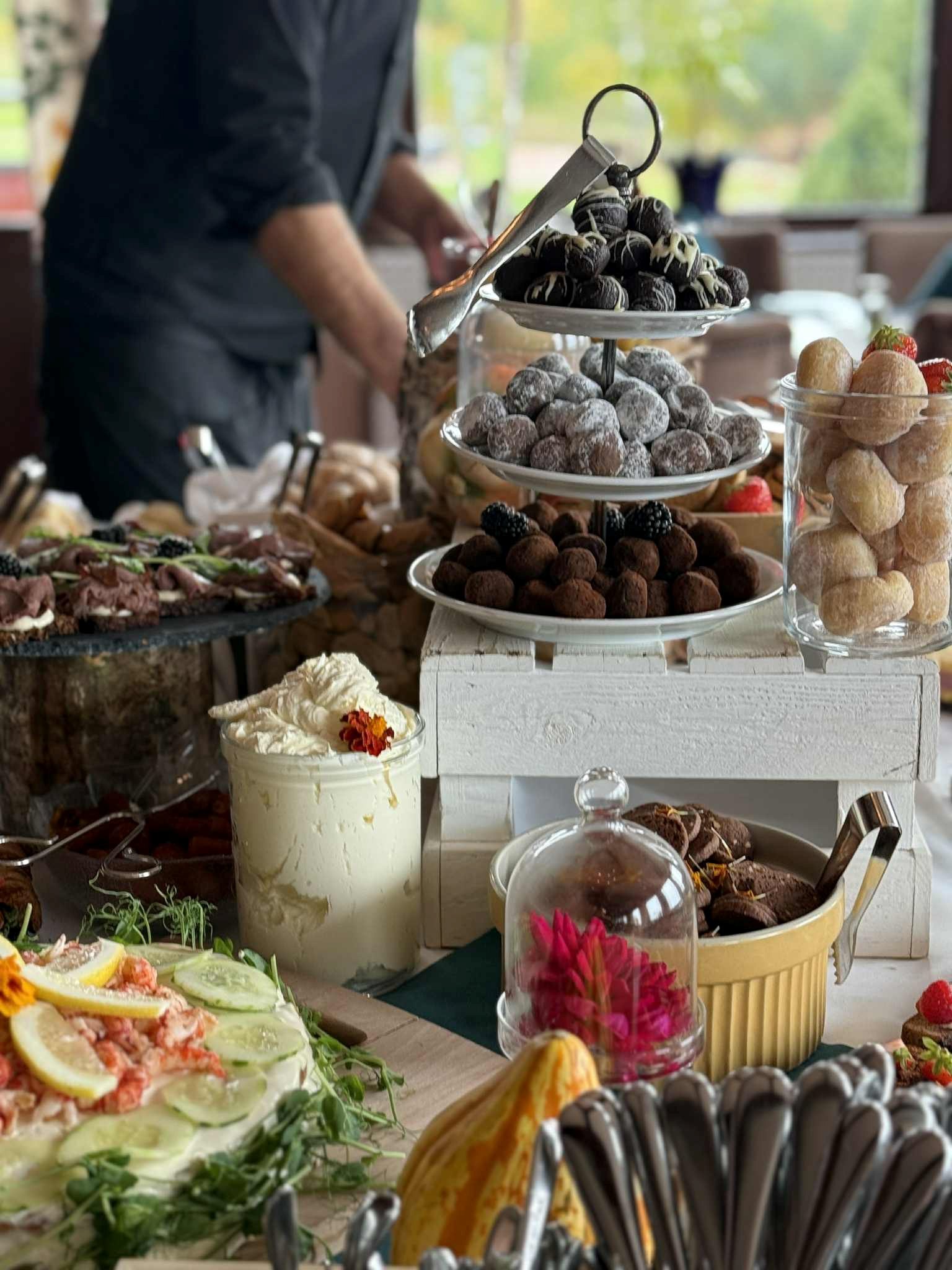 Ett bord dukat med olika desserter, bland annat en cheesecake, en chokladkaka, bakverk och ett fat med färsk blandad frukt, i en varmt upplyst matsal.